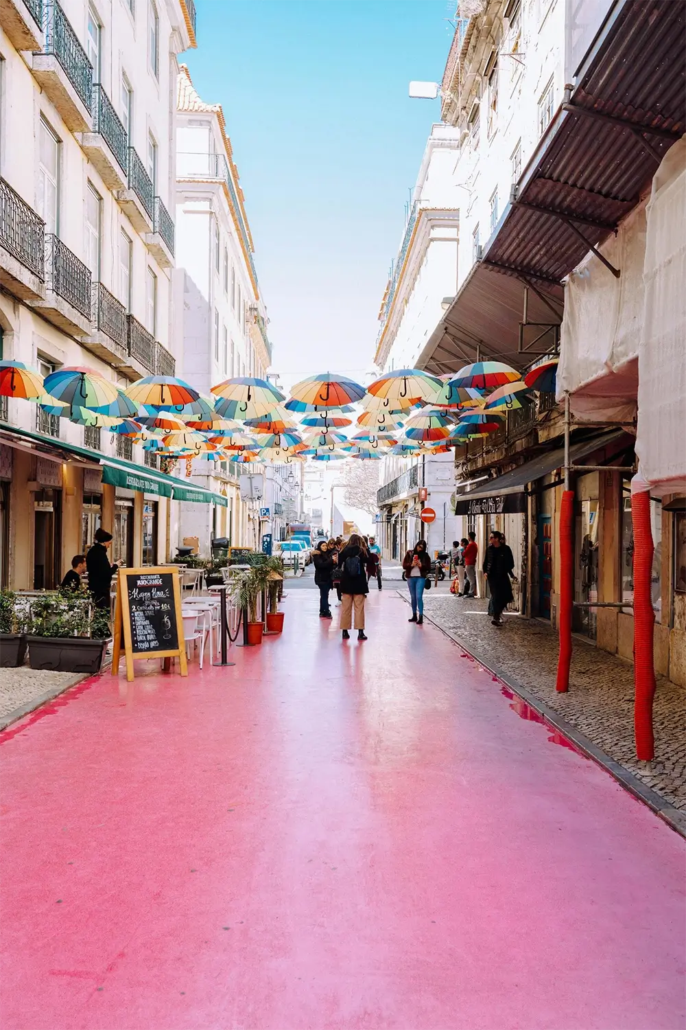 Charming Lisboa street scene featuring a pink pavement and colorful umbrellas suspended above, creating a lively atmosphere.